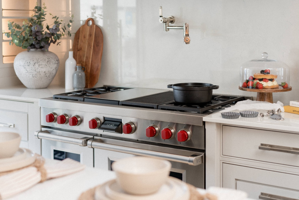 Bright modern kitchen with a Wolf range cooker featuring red knobs, marble worktop, pot filler tap, and a cake on a wooden stand