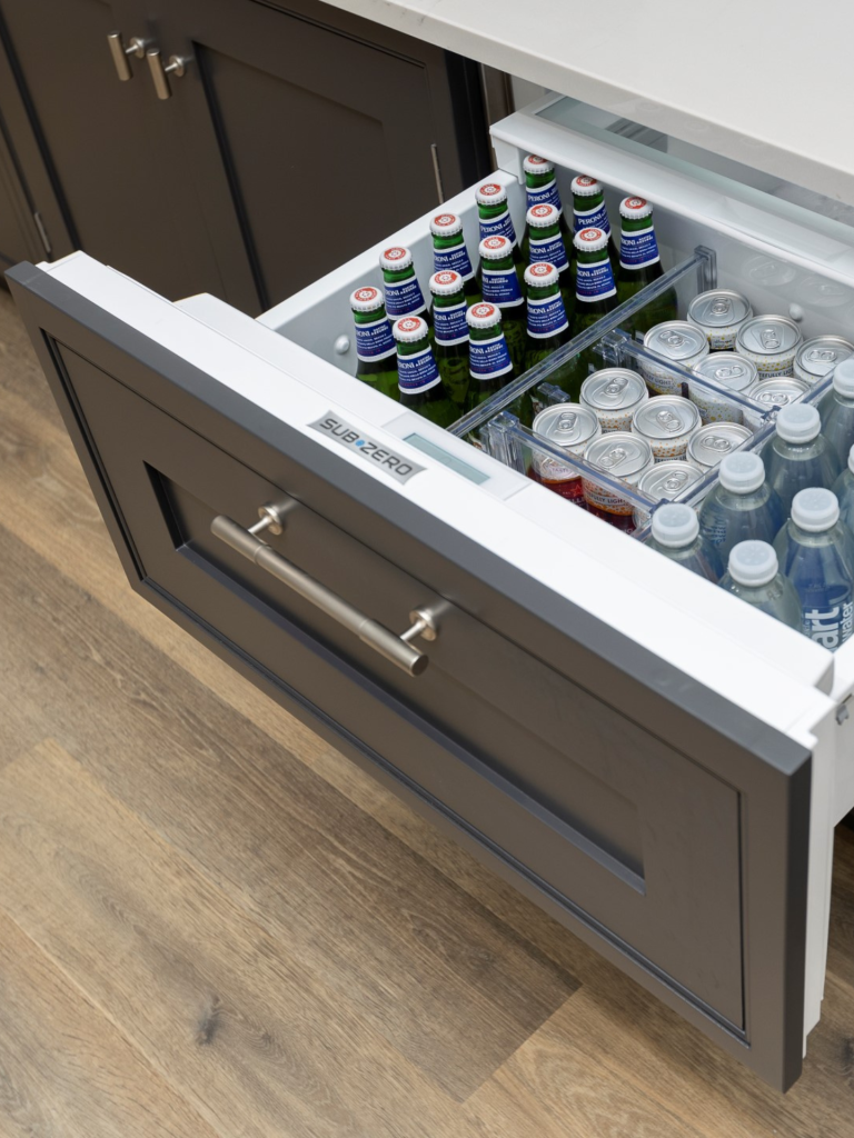 Built-in Sub-Zero refrigerator drawer in a modern kitchen island, stocked with bottled water, soft drinks, and glass bottles