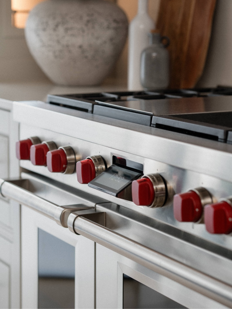 Close-up of a professional Wolf range cooker appliance with signature red knobs and stainless steel finish, styled in a luxury kitchen setting