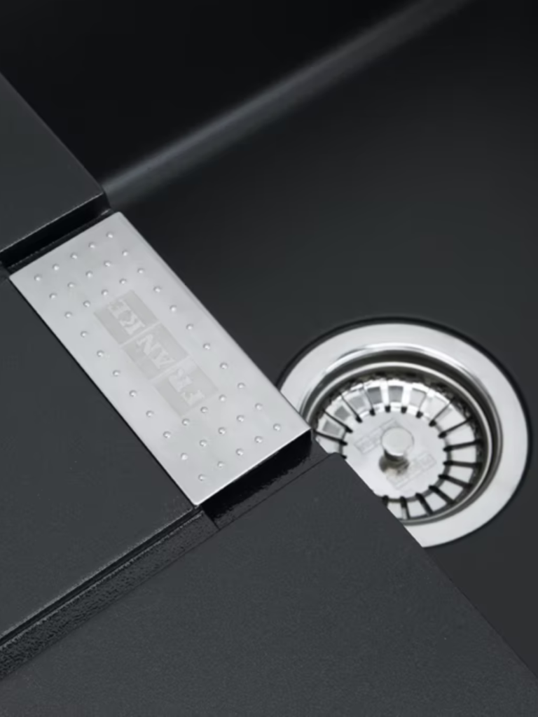 Close-up view of a modern black kitchen sink featuring a metallic inset detail with subtle textured dots and a polished stainless-steel drain strainer