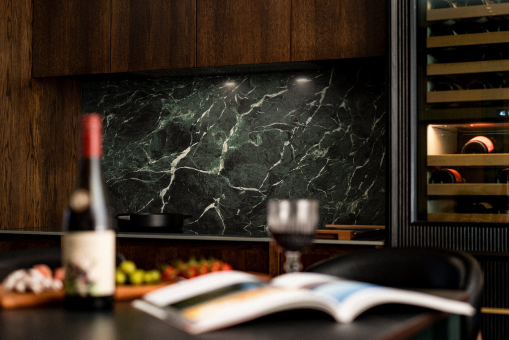 Luxury dark kitchen with green marble splashback, wooden cabinetry, integrated wine cooler, and a table set with wine and fruit