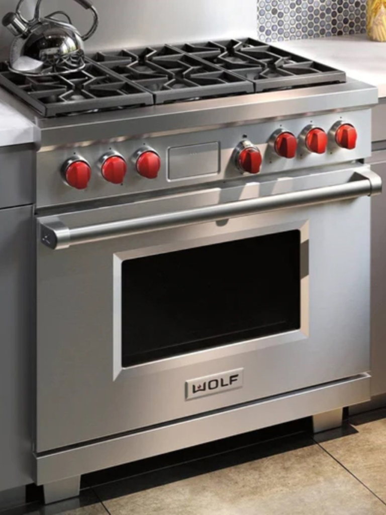 Modern Wolf stainless steel range cooker with signature red knobs, built into a sleek grey kitchen with marble countertops