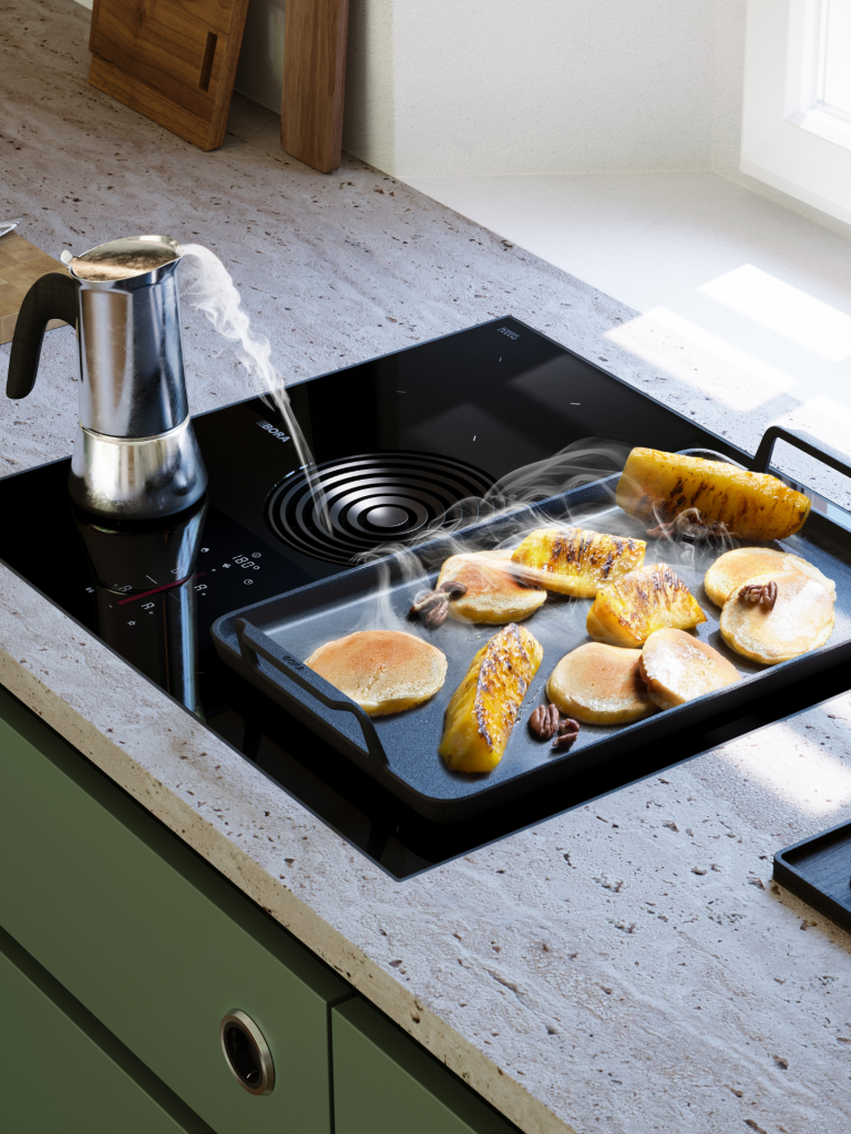 Modern kitchen with a BORA cooktop extractor and griddle cooking pancakes and pineapple slices on a stone countertop near a window