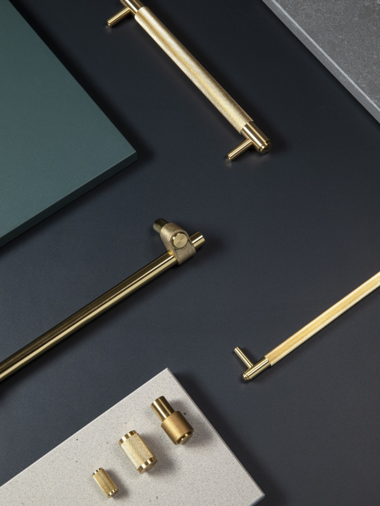Selection of luxury brass cabinet handles and fittings from Armac Martin, displayed on dark and stone surfaces in a flat lay design