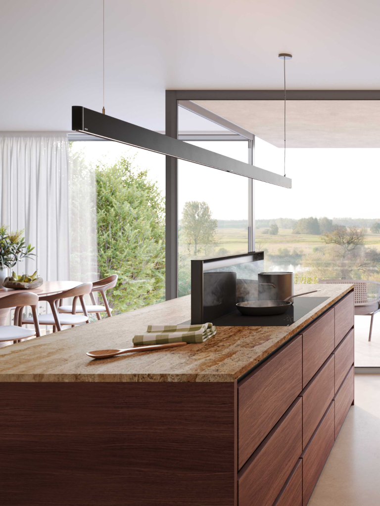 Modern kitchen island with a marble countertop and integrated downdraft extractor behind a black induction hob, set in a bright open-plan space with large windows overlooking greenery