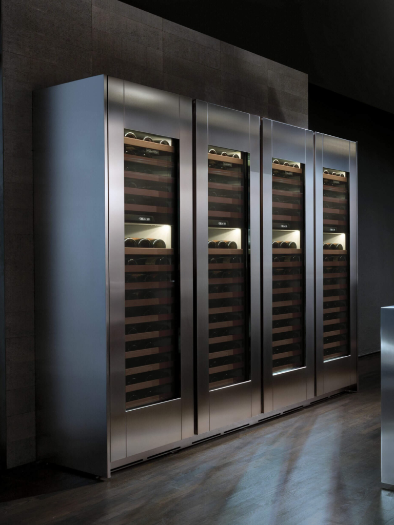 A row of tall Sub-Zero wine storage units with glass doors and wooden shelving in a dark, contemporary interior space