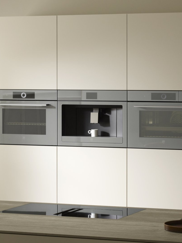 Built-in V-ZUG kitchen appliances, including ovens and a coffee machine, seamlessly integrated into a minimalist wall of cream cabinetry