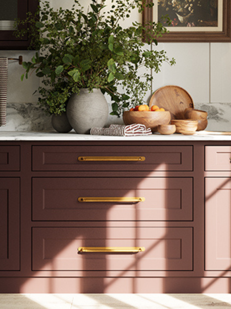 Warm-toned kitchen featuring plum-colored cabinetry with long brass drawer handles and decorative accessories on a marble countertop