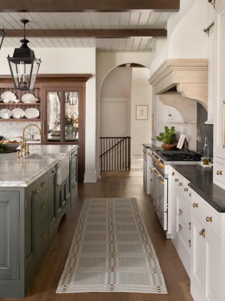 Elegant traditional kitchen with marble countertops, green and white cabinetry, brass hardware, and large lantern pendant lights, creating a warm and classic interior