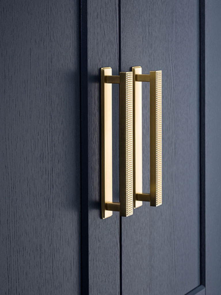 Brass textured double cabinet pull handles mounted on a dark blue shaker-style cabinet door