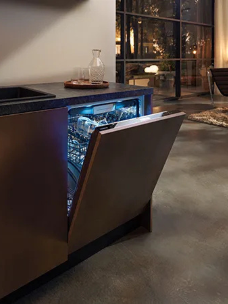 Integrated dishwasher with a wooden front panel partially open, revealing blue interior lighting and clean glassware inside a modern kitchen
