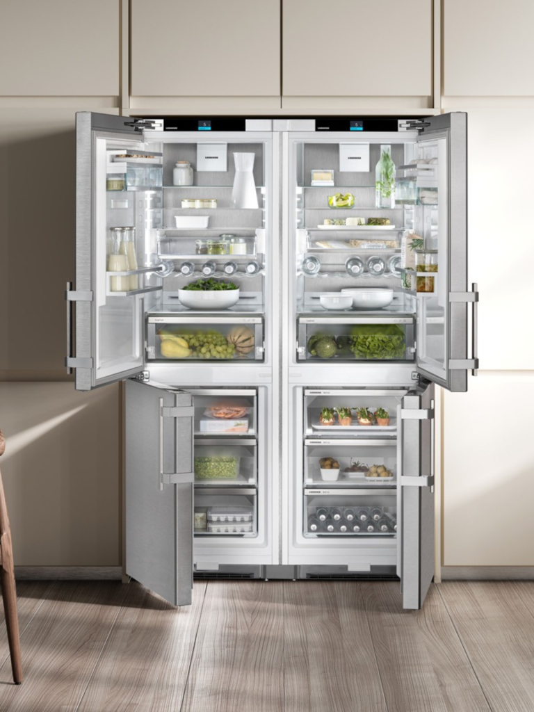 Open double-door Liebherr refrigerator showcasing neatly organised fresh produce, drinks and chilled items in a modern kitchen setting