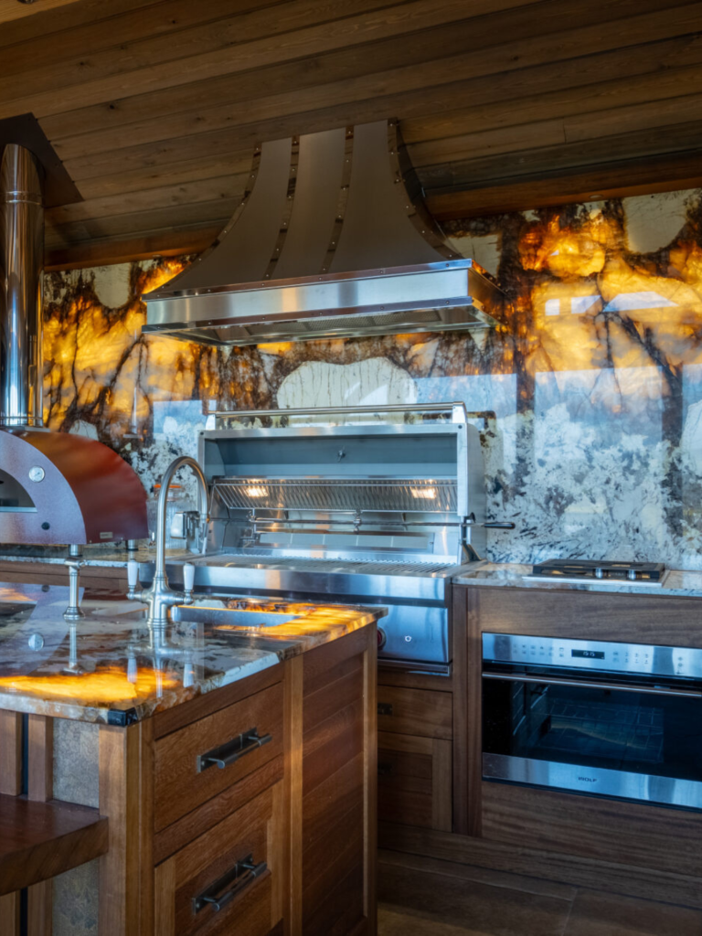 Luxury rustic kitchen with dramatic backlit stone backsplash, stainless-steel statement cooker hood, built-in grill, and rich wooden cabinetry