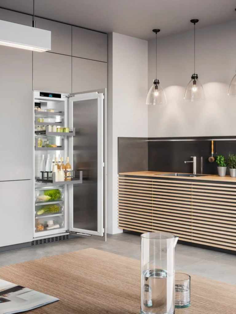Tall Liebherr refrigerator with the door open, revealing organised shelves of food and drinks in a contemporary kitchen with minimalist design