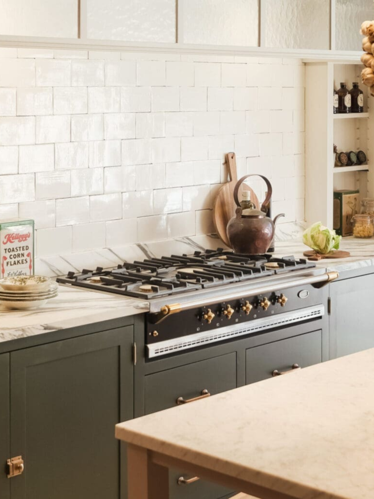 A classic Lacanche range cooker in a soft green traditional kitchen, complemented by a white tiled backsplash, marble worktop, and vintage-inspired accessories