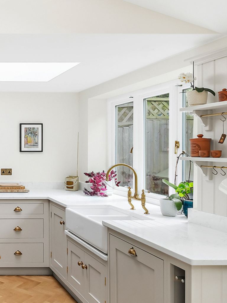 Classic kitchen with light cabinetry, white quartz worktops, and a white apron-front sink paired with a traditional gold bridge tap beneath a bright window