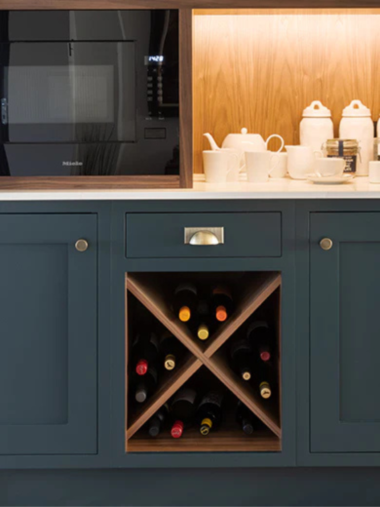 Close-up of a navy kitchen cabinet with an X-shaped wooden wine rack filled with wine bottles and warm backlighting