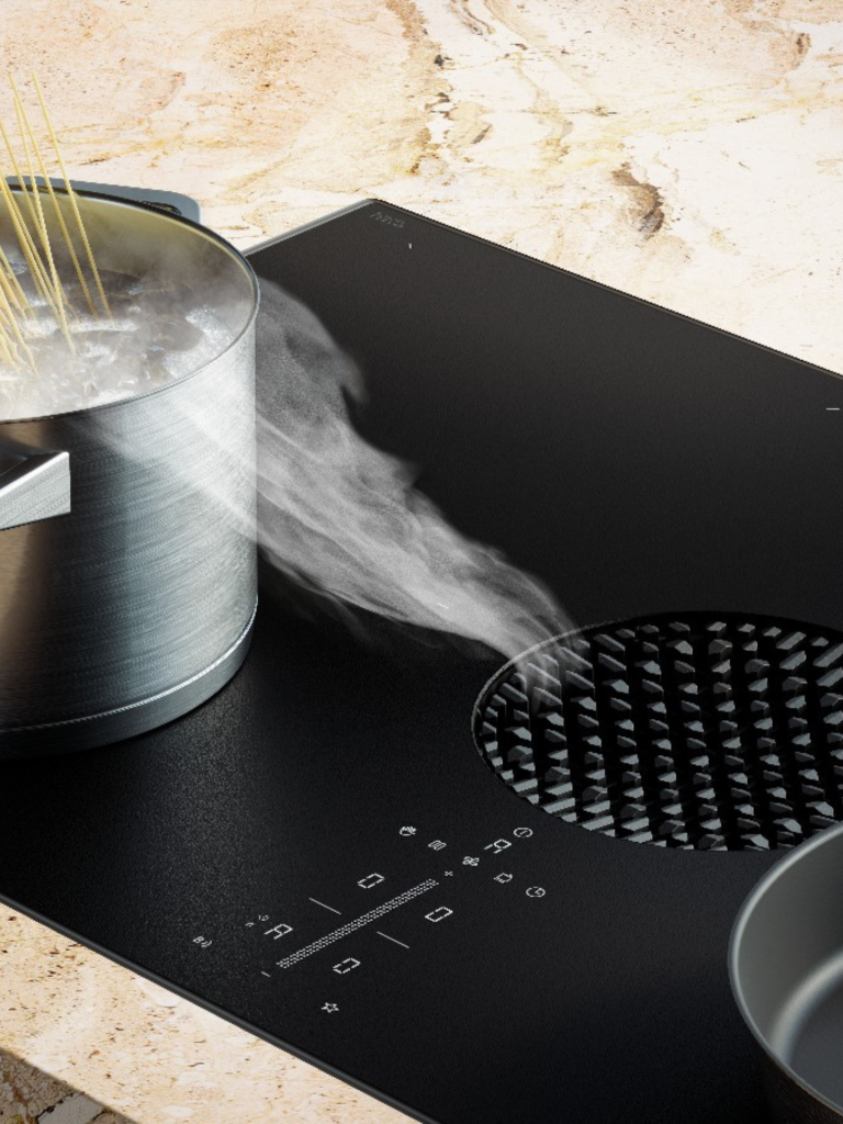 Close-up of a Bora induction hob with integrated extractor, showing steam rising from a boiling pot on a marble worktop