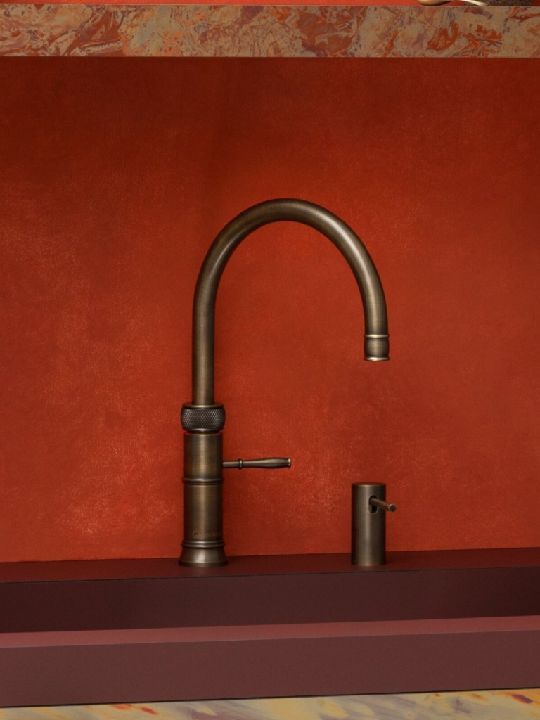 Luxury bronze Quooker tap with matching handle set against a deep red textured wall and marbled worktop surface