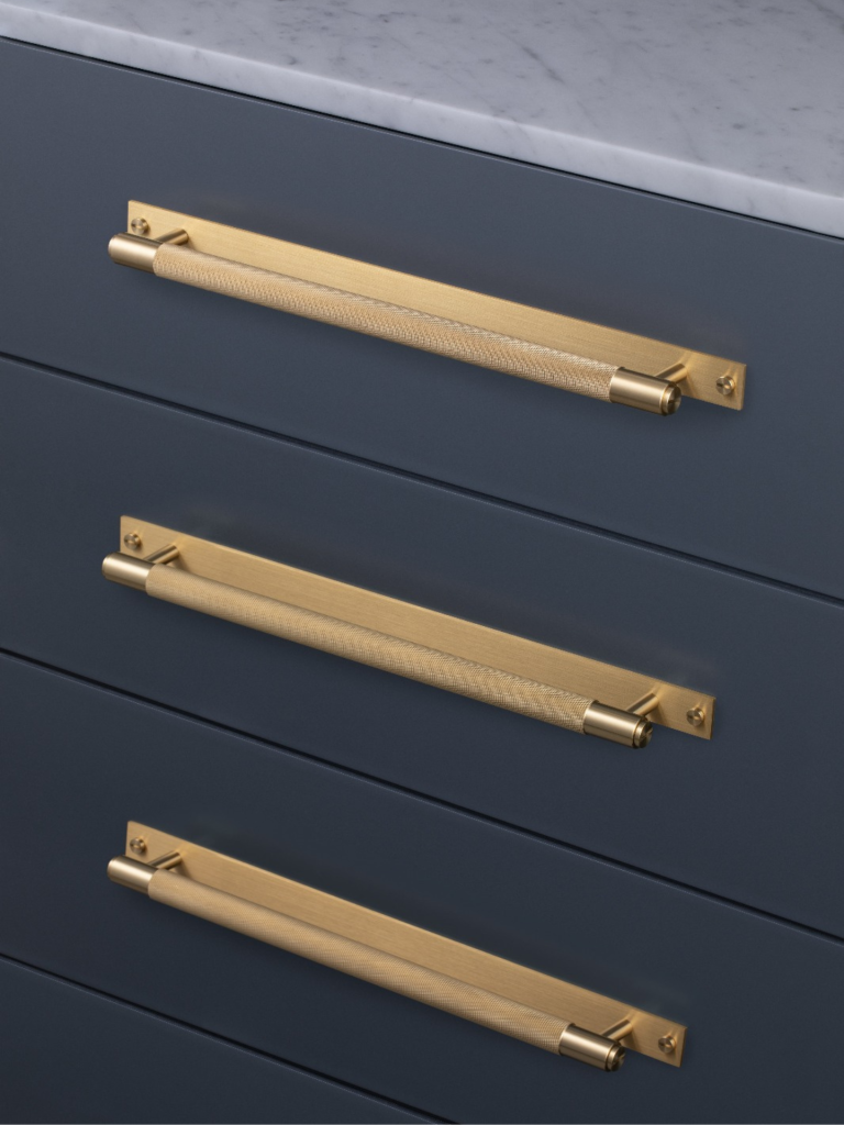 Close-up of luxury brushed brass Armac Martin cabinet handles fitted on dark blue kitchen drawers with a marble worktop above
