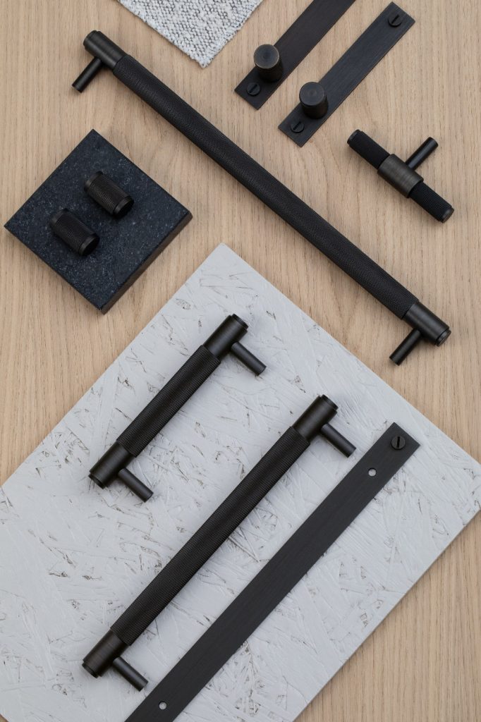 Flat lay of black knurled Buster + Punch cabinet handles and knobs displayed on wood and stone textured boards