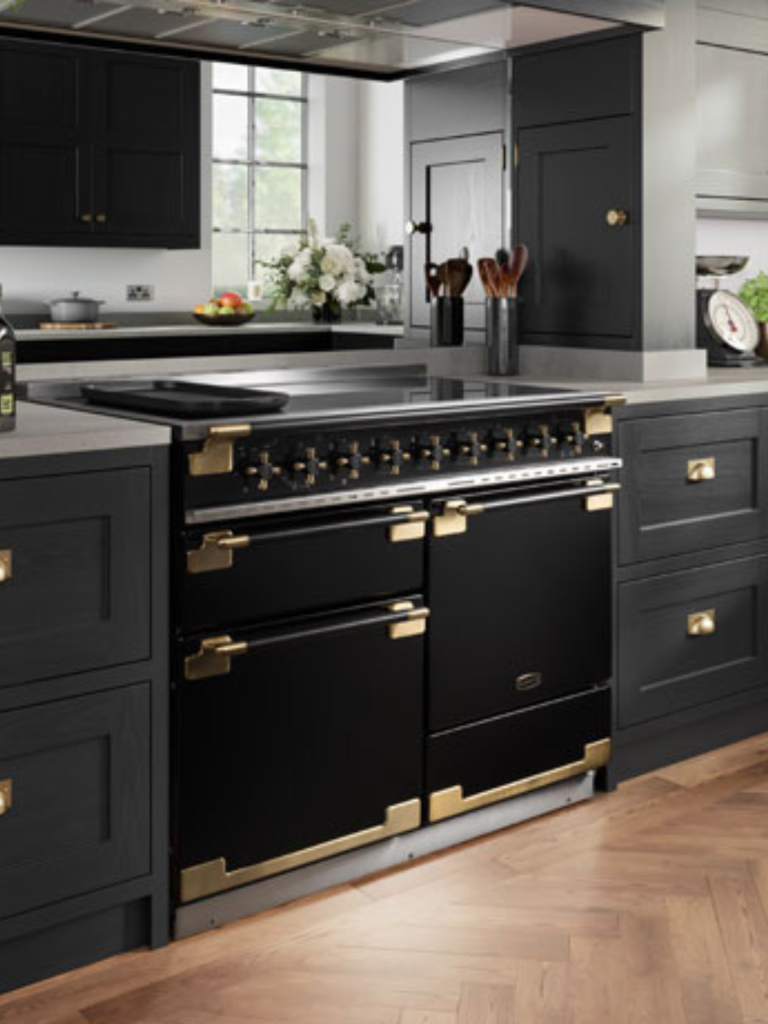 A black RangeMaster cooker with brass accents installed in a modern kitchen, surrounded by dark cabinetry and a light grey countertop